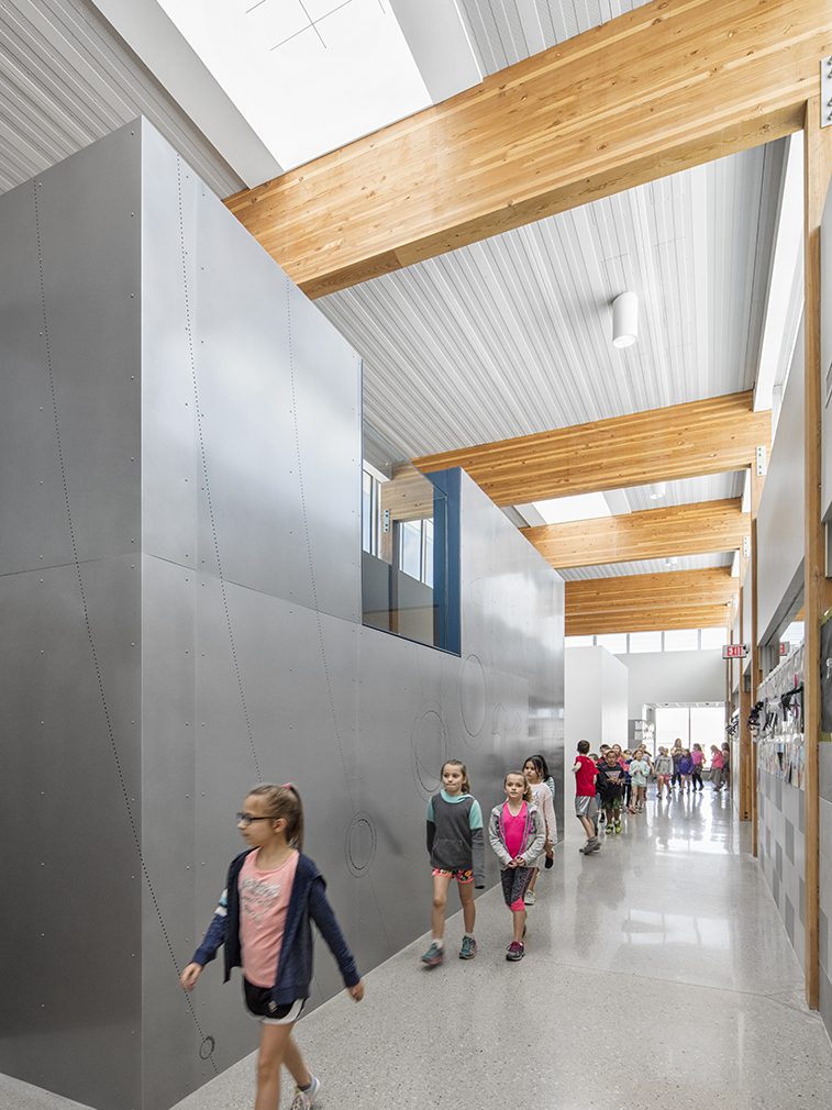 Interior of school with children walking among metal walls and wooden beams underneath Kalwall skylight system