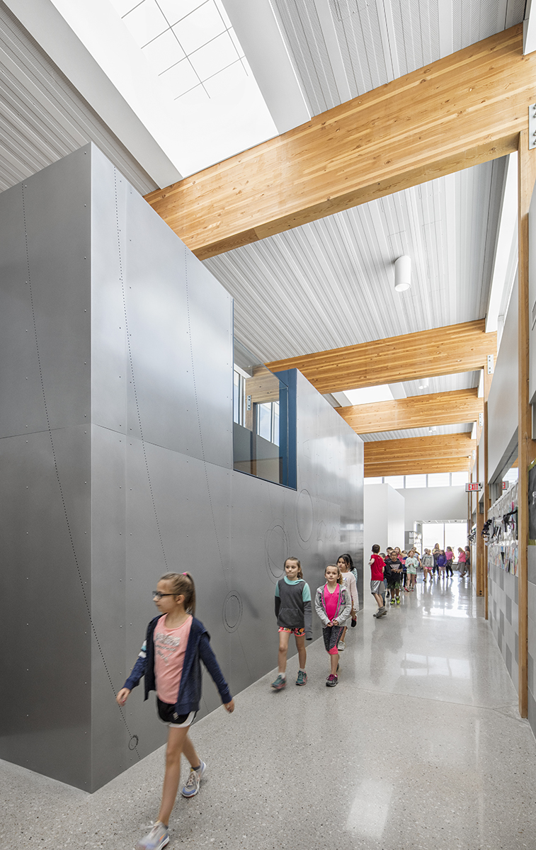 Interior of school with children walking among metal walls and wooden beams underneath Kalwall skylight system