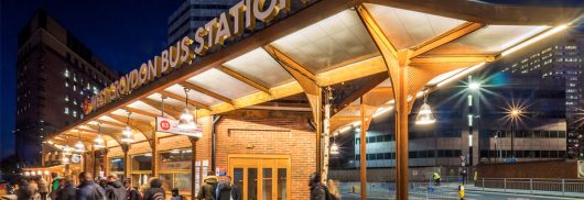 Exterior of West Croydon Bus Station at night with a Kalwall canopy system for a brick building, with a cityscape background