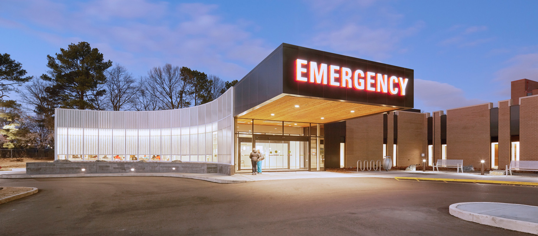 Exterior of emergency room at night time with large "Emergency" sign over entrance and curved Kalwall wall system