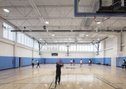 YMCA North Bronx interior w/ people playing basketball among blue and white walls and Kalwall facade on upper third of wall.