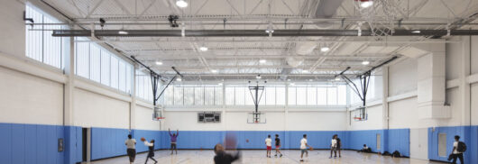 YMCA North Bronx interior w/ people playing basketball among blue and white walls and Kalwall facade on upper third of wall.