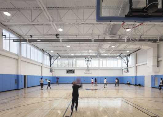 YMCA North Bronx interior w/ people playing basketball among blue and white walls and Kalwall facade on upper third of wall.