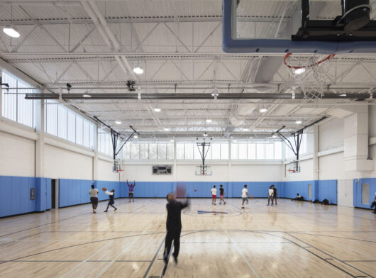 YMCA North Bronx interior w/ people playing basketball among blue and white walls and Kalwall facade on upper third of wall.