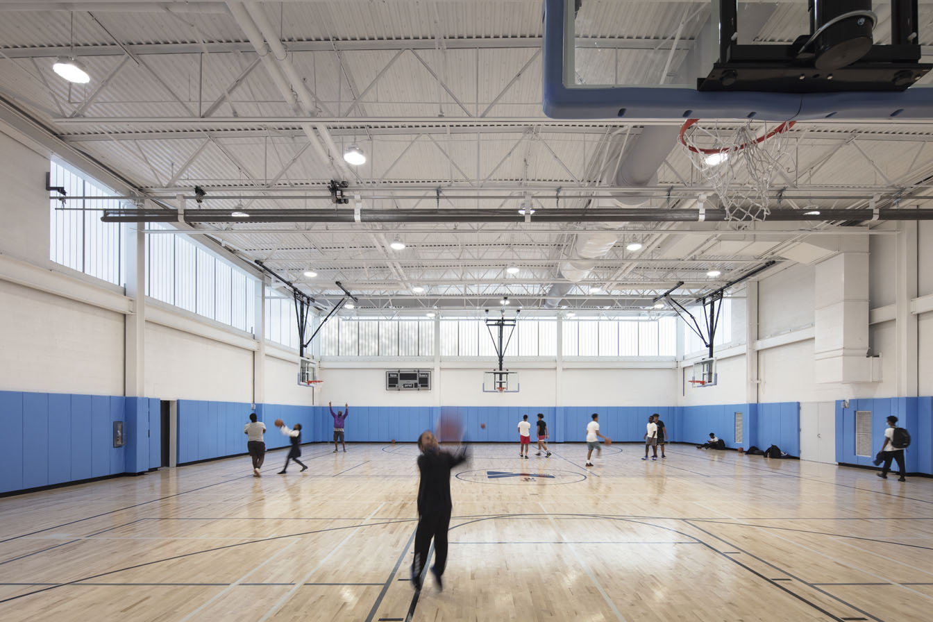 YMCA North Bronx interior w/ people playing basketball among blue and white walls and Kalwall facade on upper third of wall.