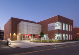 MoCo Arts building exterior at dusk featuring Kalwall facade on brick building with plants in front.