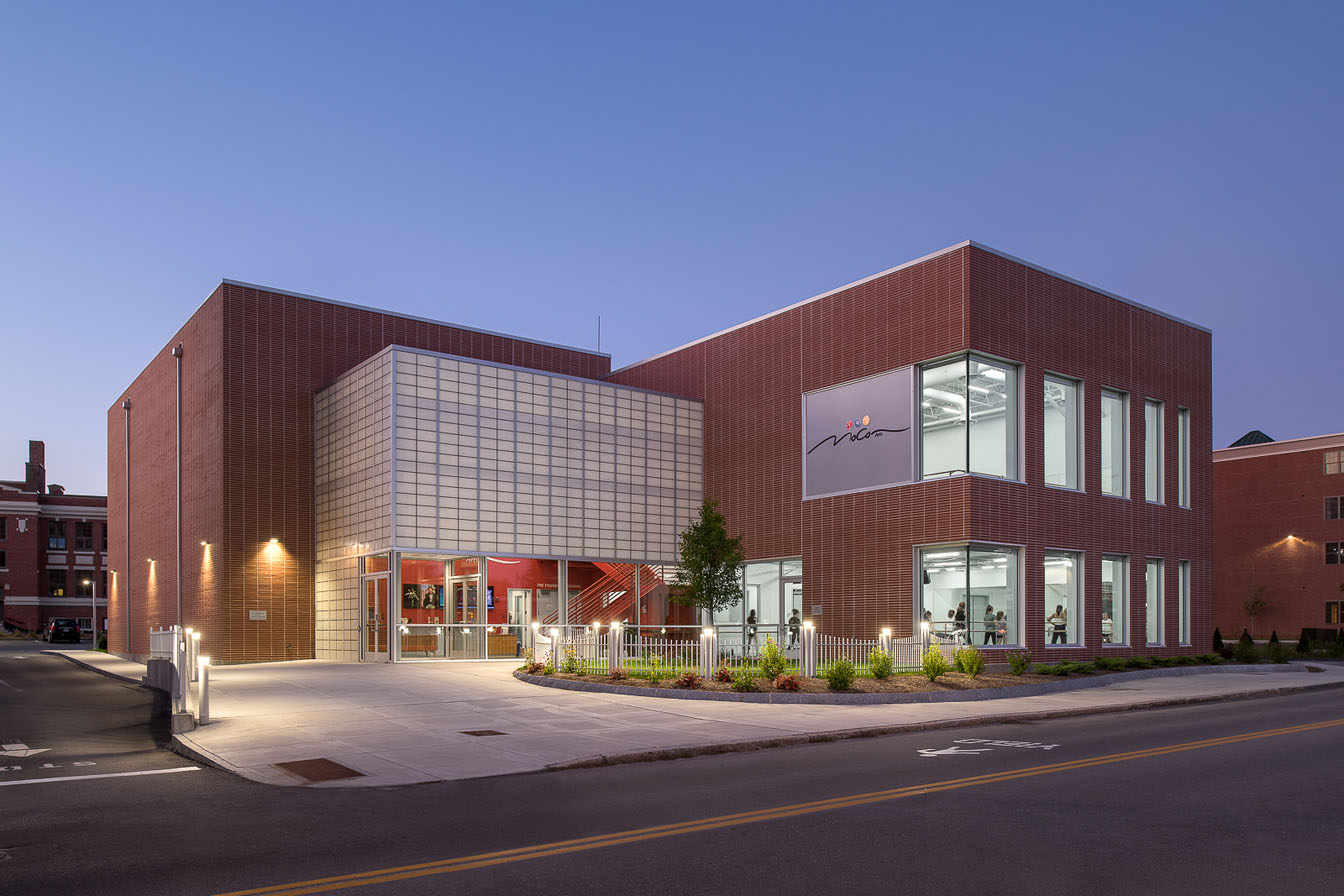 MoCo Arts building exterior at dusk featuring Kalwall facade on brick building with plants in front.