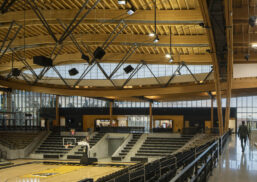 Interior of Idaho Central Credit Union gymnasium with bleachers and a curved wooden ceiling set in front of a Kalwall facade.