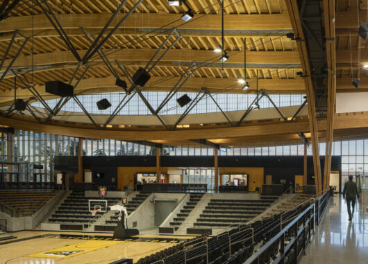 Interior of Idaho Central Credit Union gymnasium with bleachers and a curved wooden ceiling set in front of a Kalwall facade.