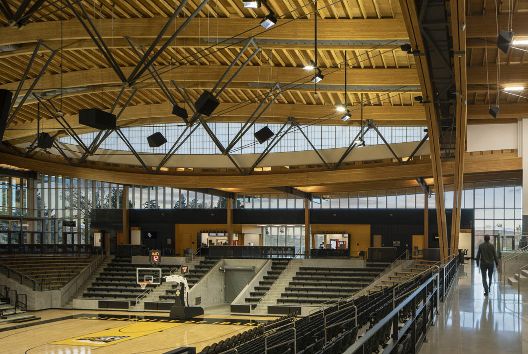 Interior of Idaho Central Credit Union gymnasium with bleachers and a curved wooden ceiling set in front of a Kalwall facade.
