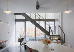 Home interior featuring a Kalwall facade above a glass wall base behind a staircase with dining table in foreground.