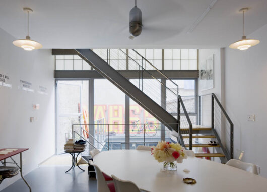 Home interior featuring a Kalwall facade above a glass wall base behind a staircase with dining table in foreground.